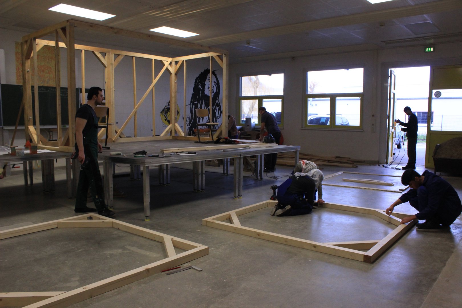 In einem großen Raum bauen Menschen massive Holzrahmen zusammen