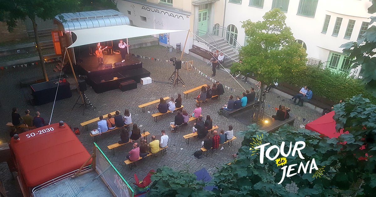 Publikum sitzt auf Bierbänken vor einer mobilen Bühne